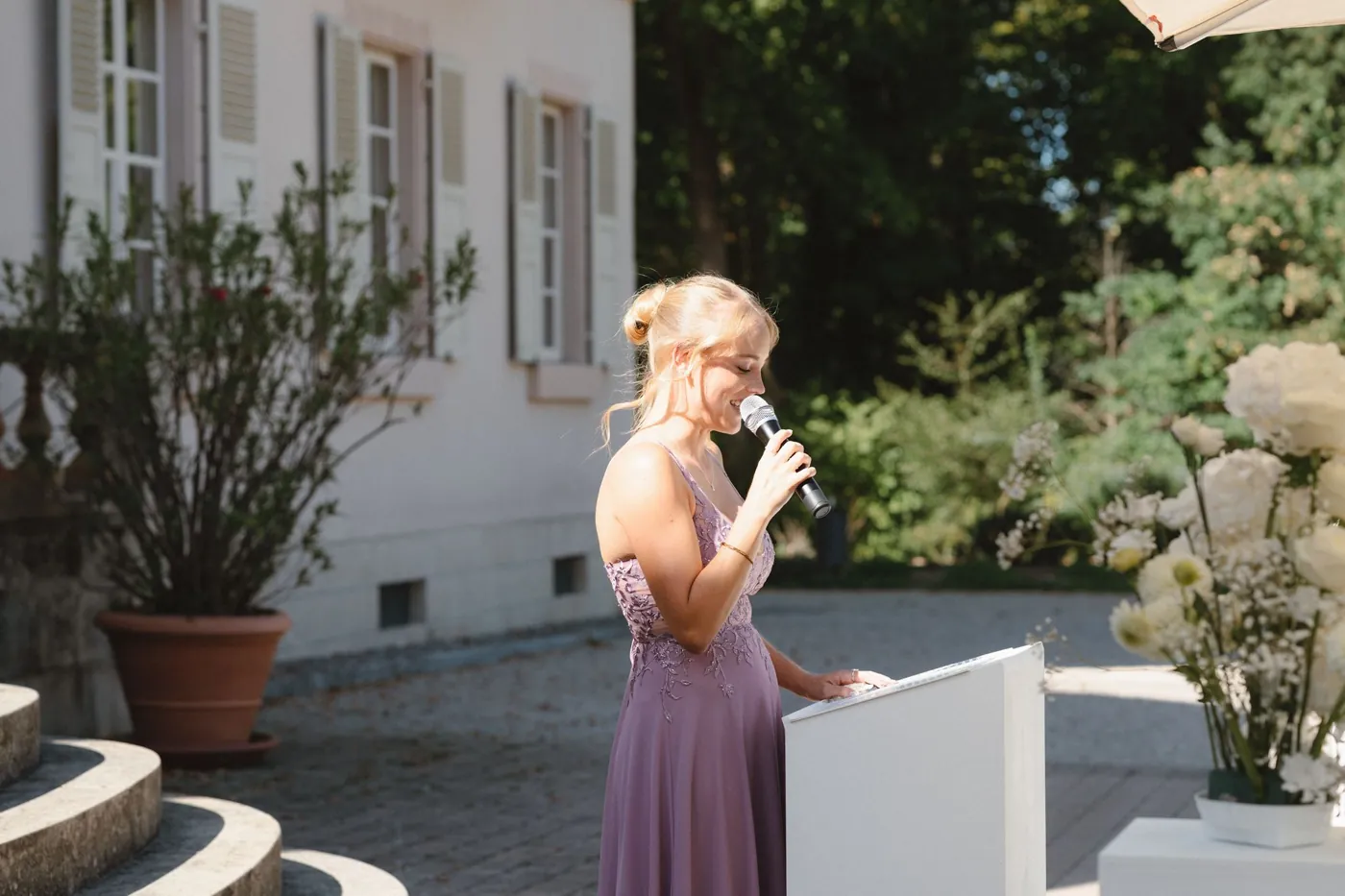 Vanessa Stamm hält lächelnd eine freie Traurede am Rednerpult im Schlossgarten